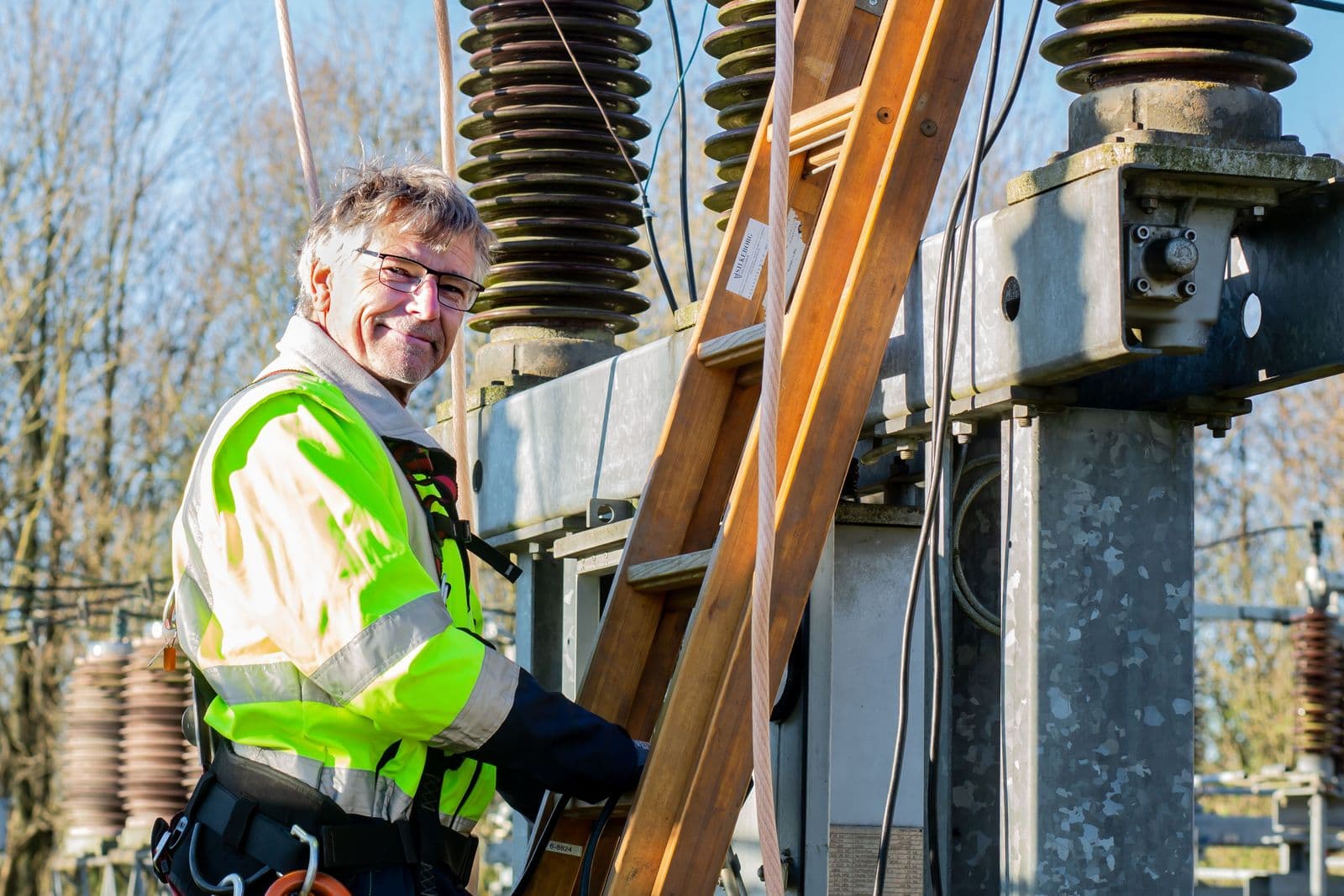 Een elektricien met een ladder bij een schakelstation